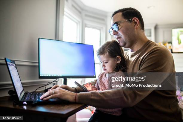 man multitasking with toddler daughter and laptop in home office - baby monitor stock-fotos und bilder