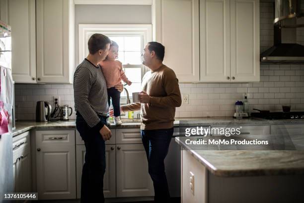 Gay couple playing with toddler daughter in kitchen