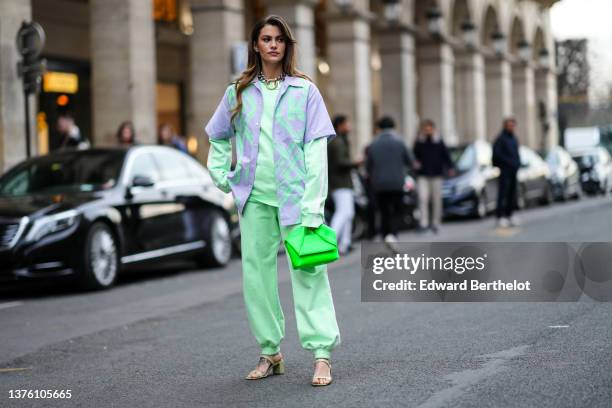 Clara Berry wears silver earrings, a large silver and gold buckle necklace, a pale green sweater, matching pale green sport pants, a pale purple and...