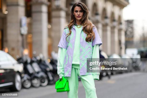 Clara Berry wears silver earrings, a large silver and gold buckle necklace, a pale green sweater, matching pale green sport pants, a pale purple and...