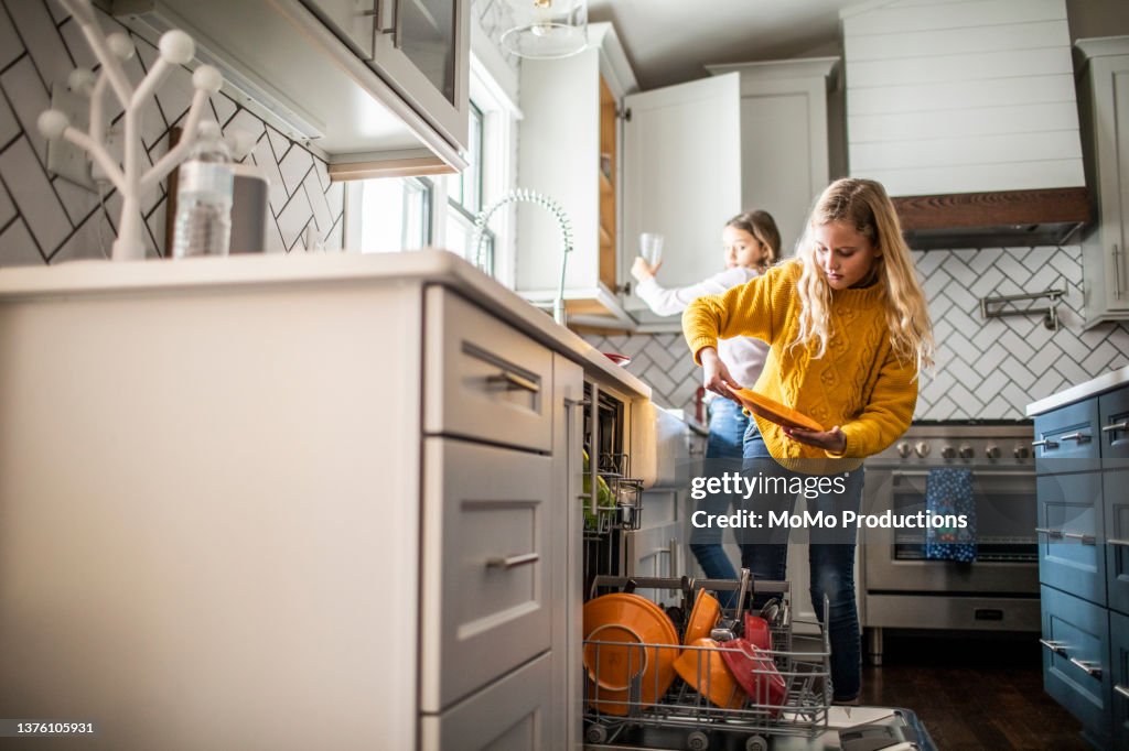 Tween girls doing dishes in modern kitchen