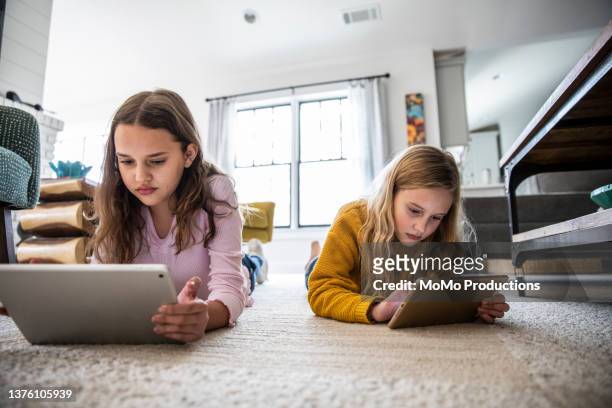 tween sisters using digital tablets on living room floor - child facebook stockfoto's en -beelden