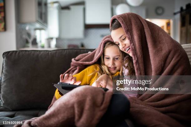 tween sisters snuggled under blanket and watching a movie on digital tablet - brown girl stock pictures, royalty-free photos & images