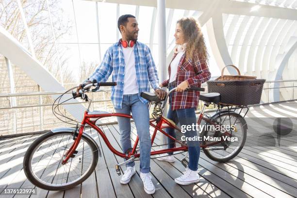 beautiful multiracial couple taking a rest on bridge after a long bike ride. - tandem stockfoto's en -beelden