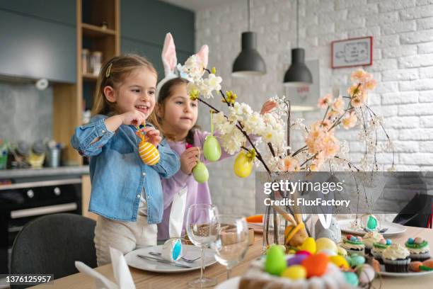 playful caucasian sisters, decorating the table for an easter lunch - easter stockfoto's en -beelden