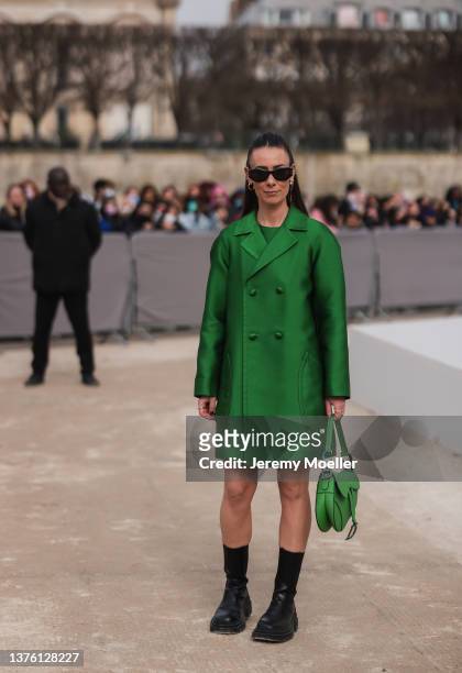 Alice Barbier wears black sunglasses, gold earrings from Dior, a green satin dress from Dior, a matching green satin buttoned coat, outside Dior,...