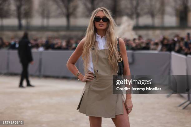 Romee Strijd wears black sunglasses, a white sleeveless shirt, a beige tank-top / pleated short dress from Dior, a black embossed print pattern...