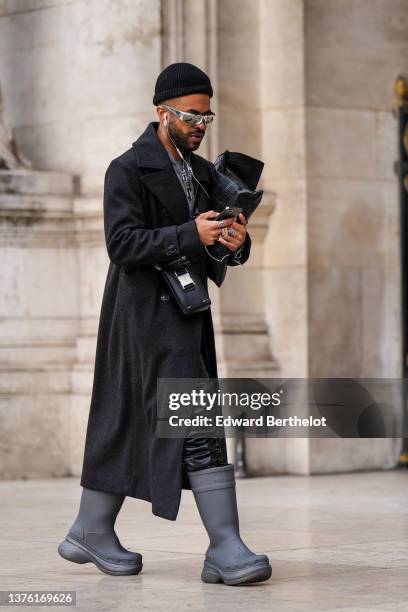 Theo Kimbaloula wears a black wool beanie, sunglasses, silver earrings, a silver chain with silver large locker pendant necklace, a gray ripped wool...