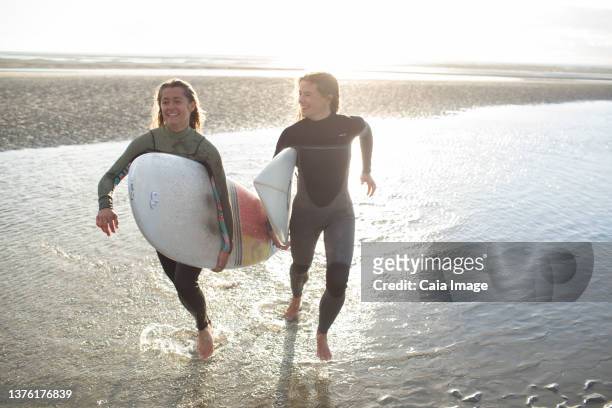 happy young female surfers running with surfboards in sunny ocean surf - beach hold surfboard stock-fotos und bilder