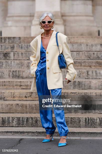 Guest wears a beige vintage sunglasses, gold with embroidered rhinestones earrings, a multicolored pearls necklace, a gold chain necklace, a white...