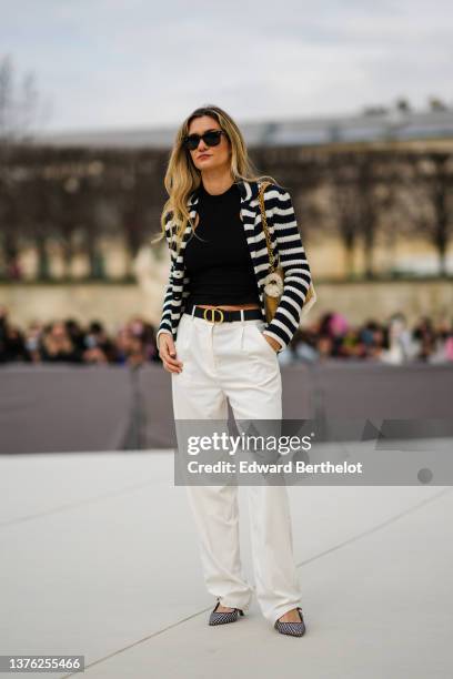 Guest wears black sunglasses from Ray Ban, a black wool tank-top, a black and white striped print pattern wool cardigan, a brown suede and white...