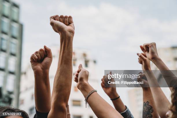 personas con los puños en alto en una manifestación en la ciudad - blm fotografías e imágenes de stock