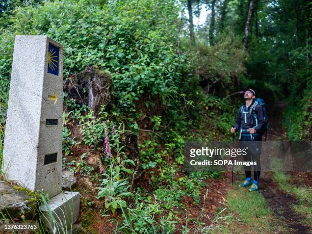 Pilgrim is seen standing next to a stone marker on the Camino de Santiago pilgrimage route. The Camino de Santiago is a large network of ancient...