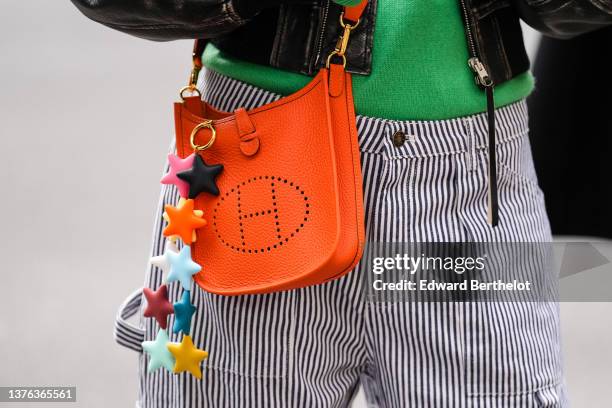 Marianne Theodorsen wears a green wool pullover, a black faded leather zipper oversized bomber coat, an orange shiny leather Evelyn crossbody bag...