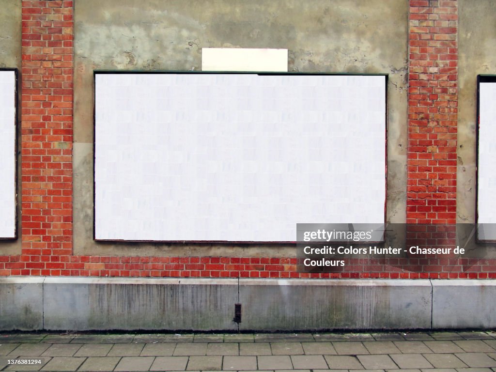 An empty billboard on a weathered wall and sidewalk in Brussels