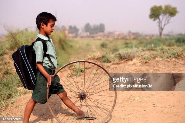 poor child running bicycle tyre on country road - indian slums stock pictures, royalty-free photos & images