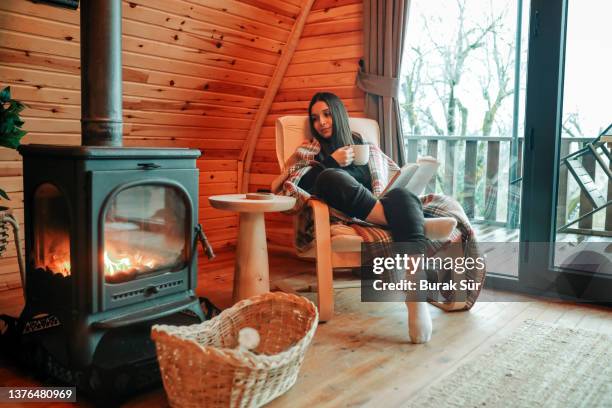 frau liest ein buch und trinkt kaffee am kamin, weibliche lifestyle freizeitaktivitäten - kaminfeuer stock-fotos und bilder