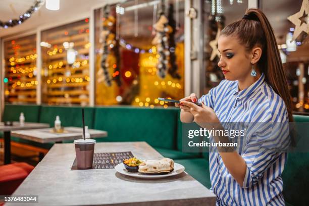 young woman taking a picture of her meal in a restaurant - fotoberichten stockfoto's en -beelden