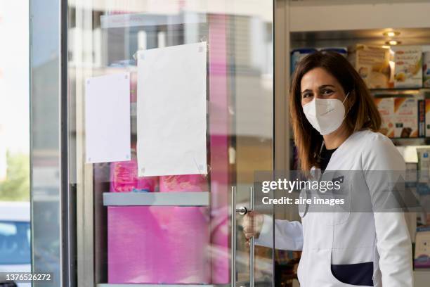 smiling brown hair woman in white uniform opening business glass door sunny day - porta de tela imagens e fotografias de stock