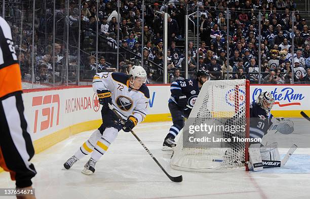 Luke Adam of the Buffalo Sabres carries the puck around the net as goaltender Ondrej Pavelec of the Winnipeg Jets keeps an eye on the play during...