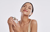 Studio shot of a young woman spraying herself with perfume