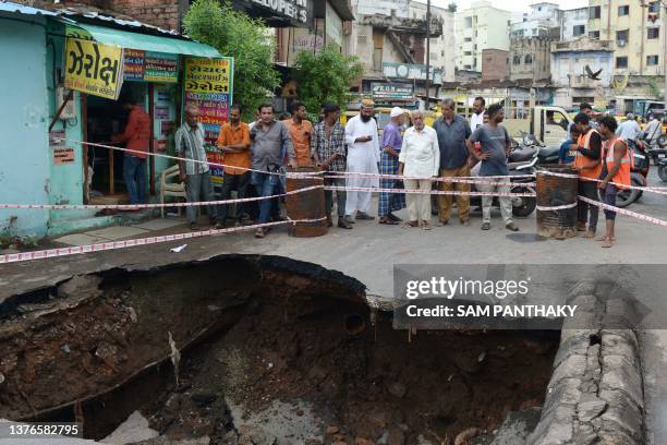 Residents gather around a caved in section of a road in Ahmedabad on July 1, 2023.