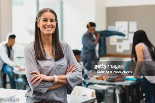 smiling female high school teacher poses for photo in classroom - portrait of teacher and student stock pictures, royalty-free photos & images