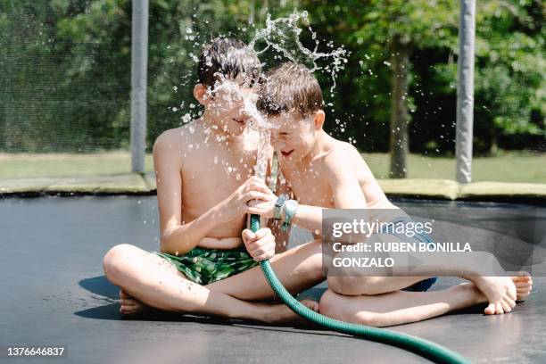 two playful kids having fun while splashing water with garden hose. recreational concept. - two kids playing with hose stock pictures, royalty-free photos & images