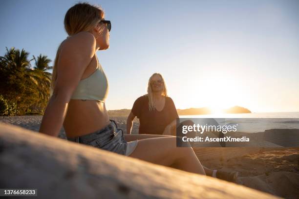 mother and daughter relax on sandy beach, at sunrise - women in daisy dukes stockfoto's en -beelden