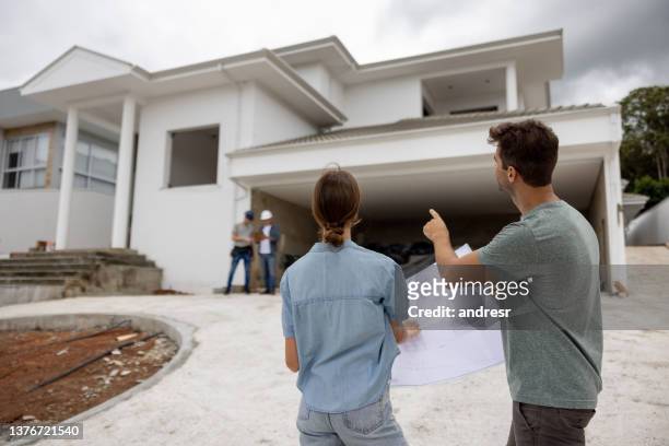 couple building their dream house and pointing at details while holding blueprint - couple pointing imagens e fotografias de stock