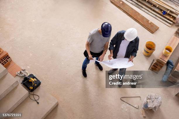 civil engineer looking at a blueprint with a worker at a construction site - rebuilding stock pictures, royalty-free photos & images