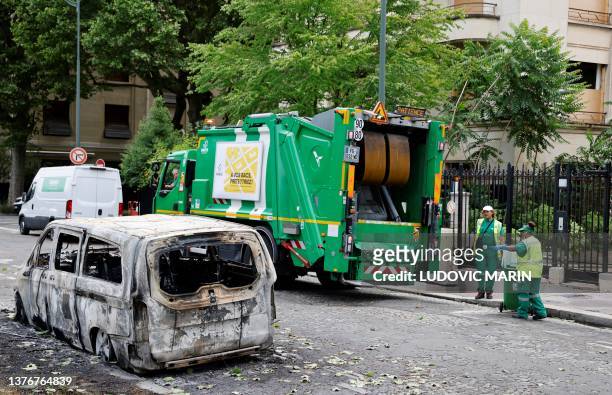 Municipal workers empty rubbish bins as they pass a burnt out vehicle in the sixth arrondisement of Paris on July 1 after continued protests...