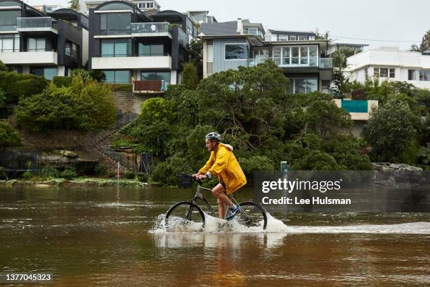 Bike rider is seen riding the flooded footpath at Manly Lagoon on March 03, 2022 in Sydney, Australia. Thousands are being told to evacuate Sydney...