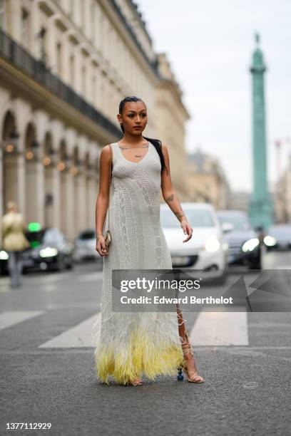 Guest wears gold earrings, a gray cut-out pattern tank-top / long dress with yellow feathers borders, a beige shoulder bag, yellow leather strappy /...