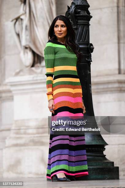 Guest wears silver and rhinestones earrings, a green / yellow / purple / pink / orange / black striped print pattern long sleeves long dress, black...