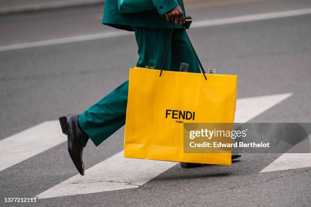 Guest wears a green blazer jacket, matching green suit pants, a green shiny leather crossbody bag from Prada, a yellow oversized shopping bag from...