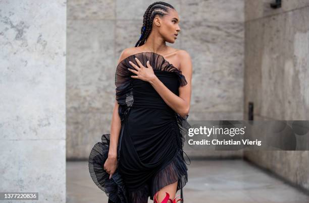 Cindy Bruna seen with braids wearing asymmetric black laced sheer off shoulder dress, red yellow fire print over knees cut out boots outside Rochas...