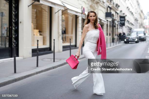 Influencer Alexandra Lapp wearing a white Colette feather jumpsuit by Nadine Merabi, a pink tweed jacket by Valentino, a silver chain crystal belt by...