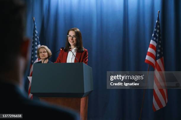 dark haired female politician during the speech on a blue background with american flags - mayor office stock pictures, royalty-free photos & images