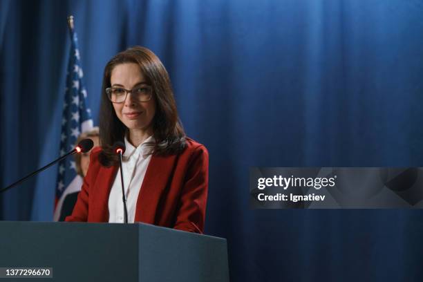 amerikanische politikerin in roter jacke, die während der rede in die kamera lächelt - global press conference stock-fotos und bilder