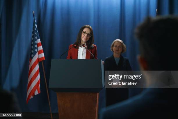 female dark haired american politician giving a speech at the debate, standing on a blue background with american flag - president desk stock pictures, royalty-free photos & images