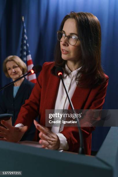 dunkelhaarige amerikanische politikerin in roter jacke beantwortet die fragen nach ihrer rede - global press conference stock-fotos und bilder
