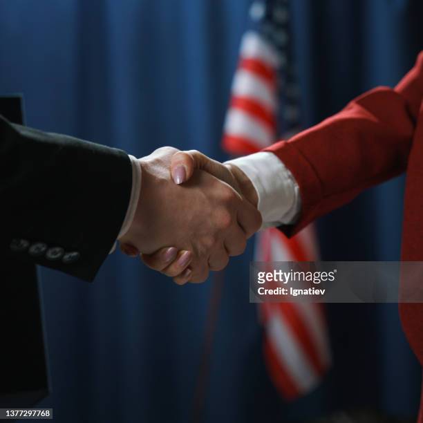primo piano di una stretta di mano di un uomo e una donna politici su sfondo blu con una bandiera degli stati uniti - us ambassador foto e immagini stock