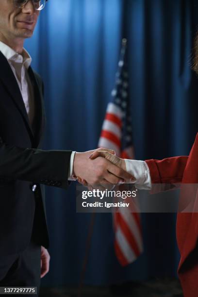 a handshake of two politicians after negotiations on a blue background with a us flag - ambassador stock pictures, royalty-free photos & images