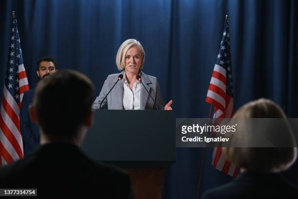 blond female politician giving a speech at the debates, standing on a stage with blue background - american flag on stage stock pictures, royalty-free photos & images