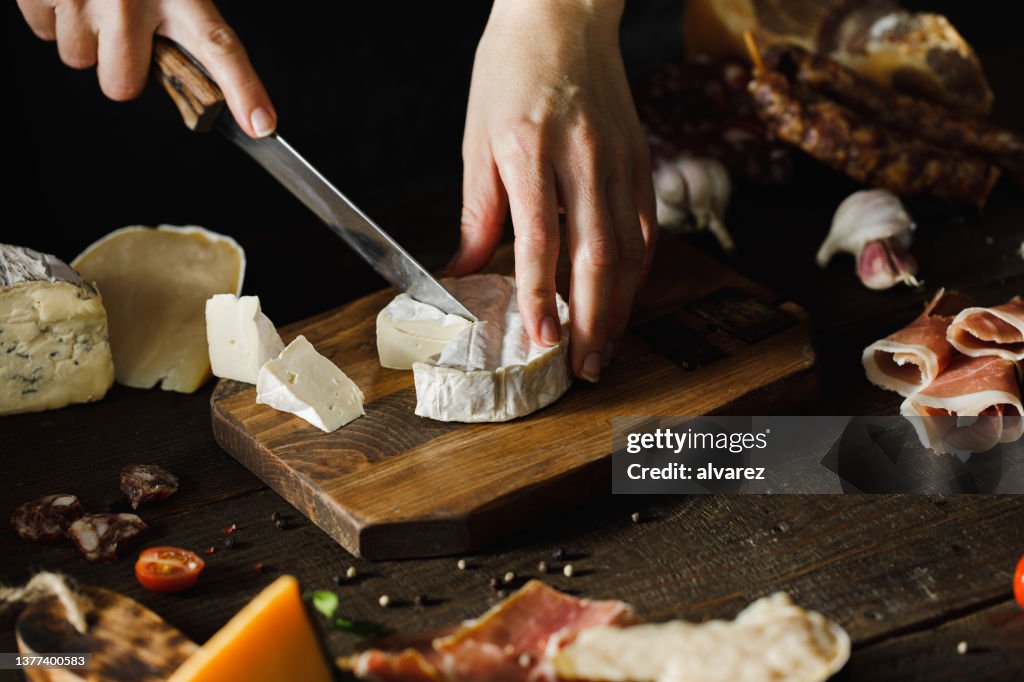 Woman hand cutting camembert on wooden board