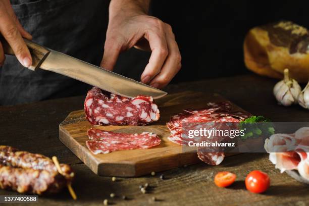 manos de mujer cortando salchicha de salami en tabla de madera - charcutería fotografías e imágenes de stock