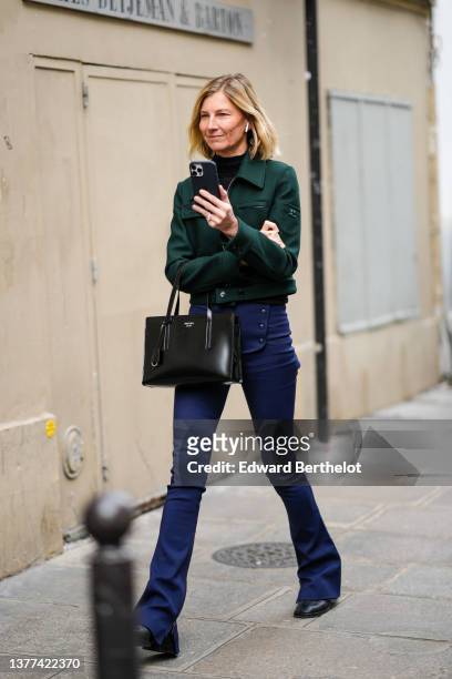 Guest wears a black turtleneck pullover, a dark green jacket from Courreges, a black shiny leather handbag from Prada, navy blue buttoned waist /...
