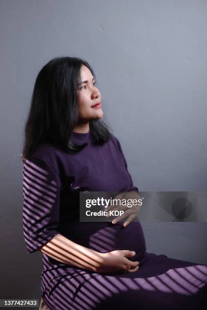 pregnant woman holding her belly in studio shot. - studio shot lonely woman stock pictures, royalty-free photos & images