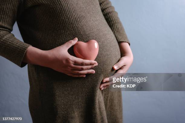 pregnant woman holding her belly and heart shape in studio shot. - studio shot lonely woman stock-fotos und bilder